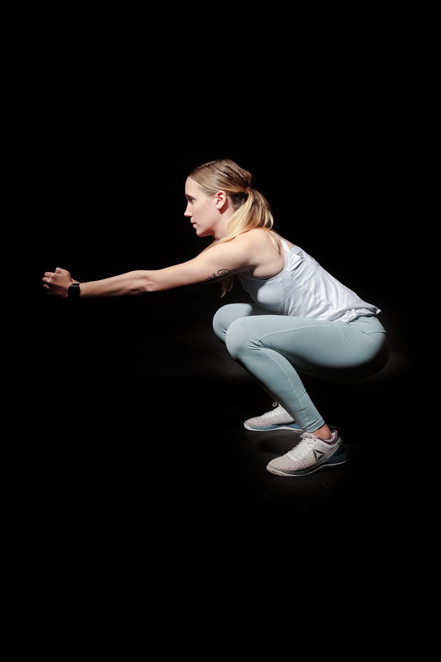side view photo of woman doing squats against black background