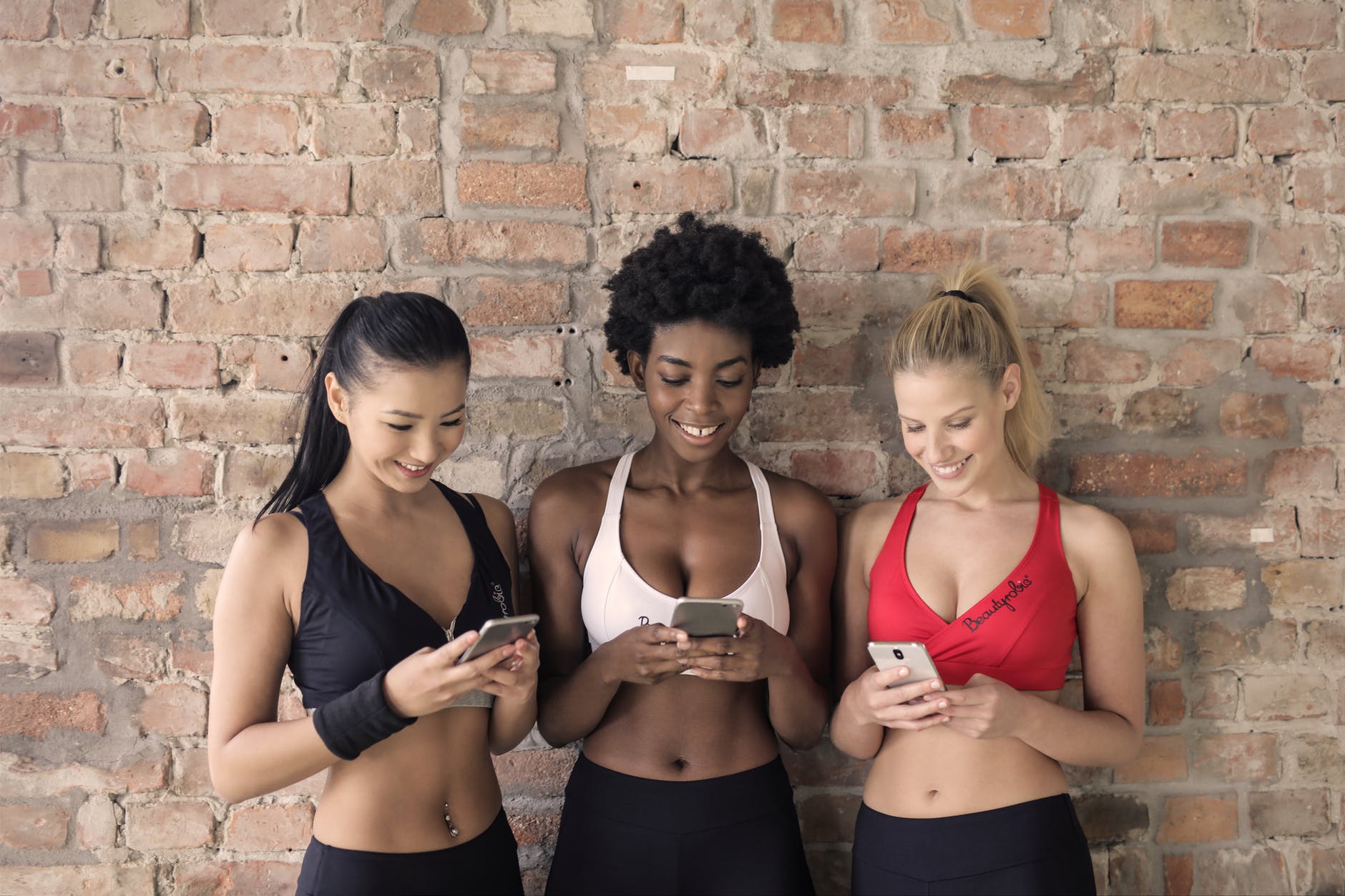 three woman in assorted color sport bras holding and watching their smartphones