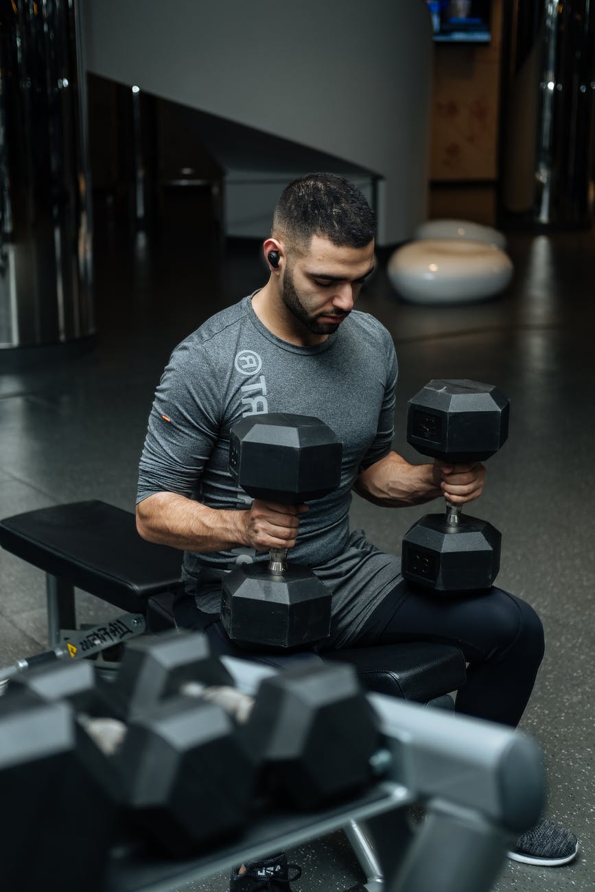 man sitting on flat bench while holding two dumbbells