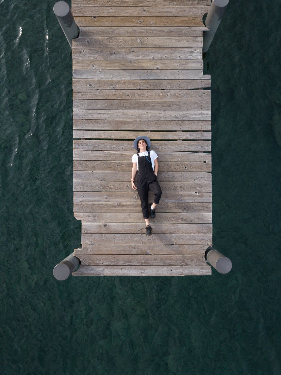 woman in black overall lying down on wooden dock