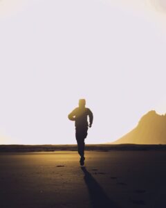 silhouette of unrecognizable man running on sand at sunset